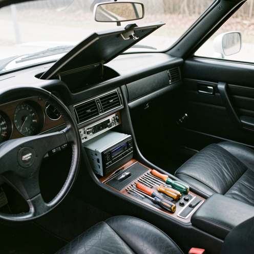 Console centrale d’un coupé européen ancien ouverte pour l’installation d’un nouvel autoradio, avec des outils soigneusement disposés dans l’habitacle.