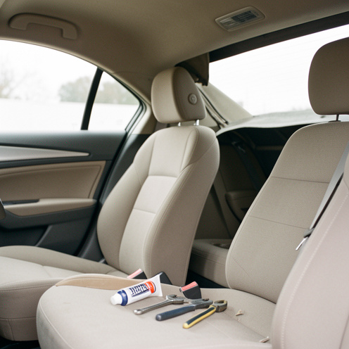 Intérieur d’une voiture avec le tissu du ciel de toit partiellement décollé, accompagné d’un tube de colle automobile et d’outils de réparation.