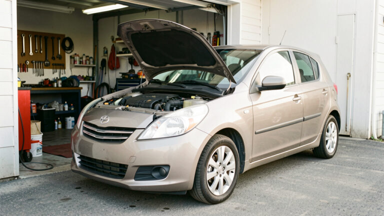 Voiture compacte d’occasion bien entretenue devant un garage, avec des outils et des fournitures de maintenance soigneusement rangés.