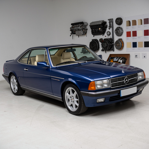 Coupé français élégant de la fin des années 1990, présenté dans un studio automobile avec une carrosserie bleu métallisé, un intérieur en cuir clair, des jantes alliage et des éléments techniques visibles en arrière-plan.